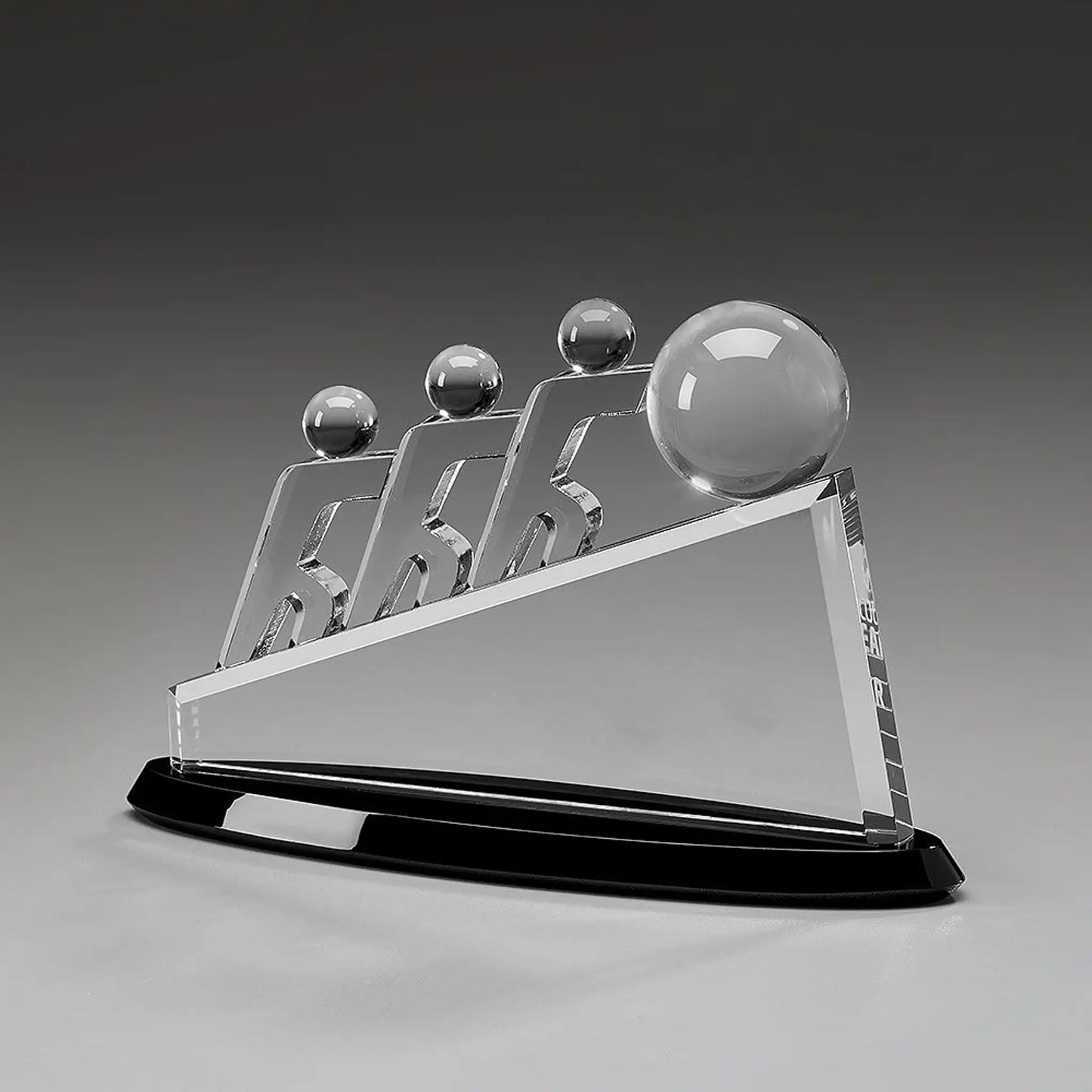 Collaboration Award aus Kristallglas – drei aufstrebende Figuren mit großer Glaskugel auf dreieckigem Glaskörper und schwarzem Sockel, Höhe 145 mm – hier ohne Gravur

