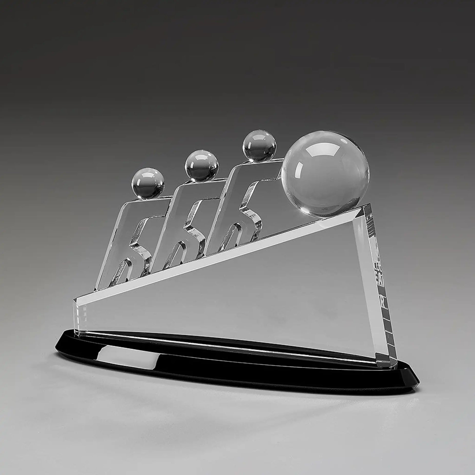 Collaboration Award aus Kristallglas – drei aufstrebende Figuren mit großer Glaskugel auf dreieckigem Glaskörper und schwarzem Sockel, Höhe 145 mm – hier ohne Gravur
