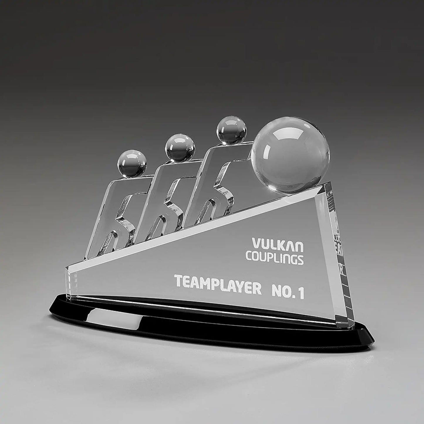 Collaboration Award aus Kristallglas – drei aufstrebende Figuren mit großer Glaskugel auf dreieckigem Glaskörper und schwarzem Sockel, Höhe 145 mm – mit Beispielgravur „Teamplayer No. 1"
