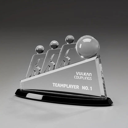 Collaboration Award aus Kristallglas – drei aufstrebende Figuren mit großer Glaskugel auf dreieckigem Glaskörper und schwarzem Sockel, Höhe 145 mm – mit Beispielgravur „Teamplayer No. 1"
