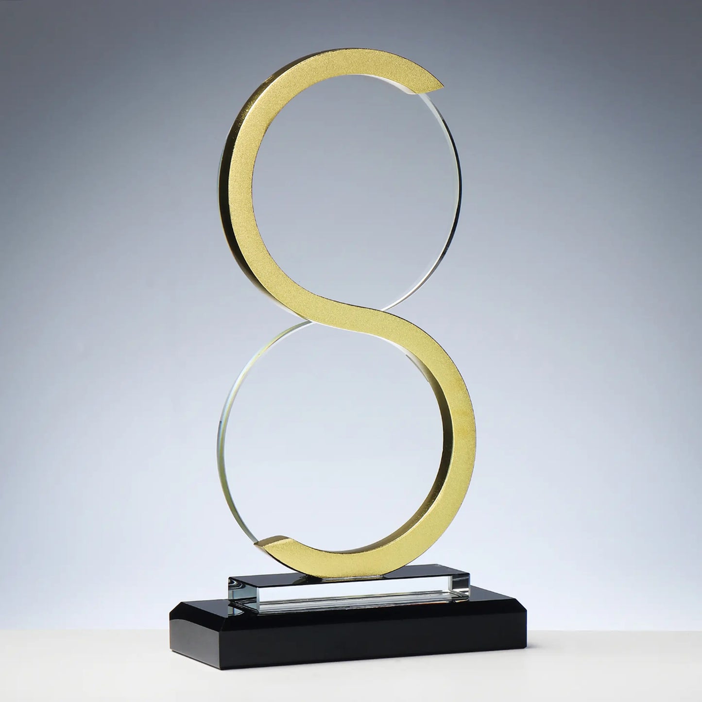 Glas-Metall Award GOLDEN INFINITE – geschwungene Doppelring-Skulptur in Gold-Metall auf schwarzem Glassockel, Unendlichkeits-Symbol-Form, blank ohne Gravur, personalisierbar mit Lasergravur für Unternehmensauszeichnungen und Gala-Abende
