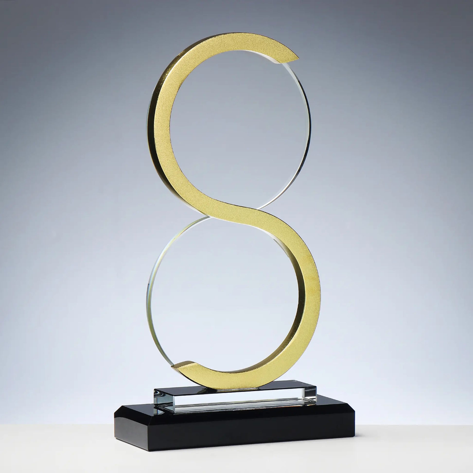 Glas-Metall Award GOLDEN INFINITE – geschwungene Doppelring-Skulptur in Gold-Metall auf schwarzem Glassockel, Unendlichkeits-Symbol-Form, blank ohne Gravur, personalisierbar mit Lasergravur für Unternehmensauszeichnungen und Gala-Abende
