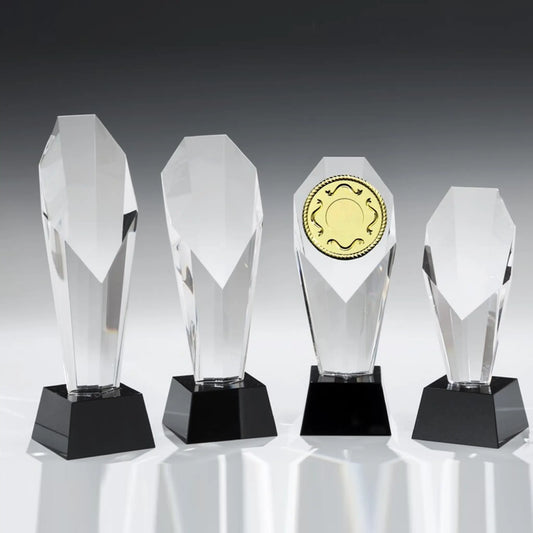 Monument Tower Award aus klarem Kristallglas in vier Größen – facettierte Kristallstele auf schwarzem Glassockel, eine Variante mit goldenem Emblem
